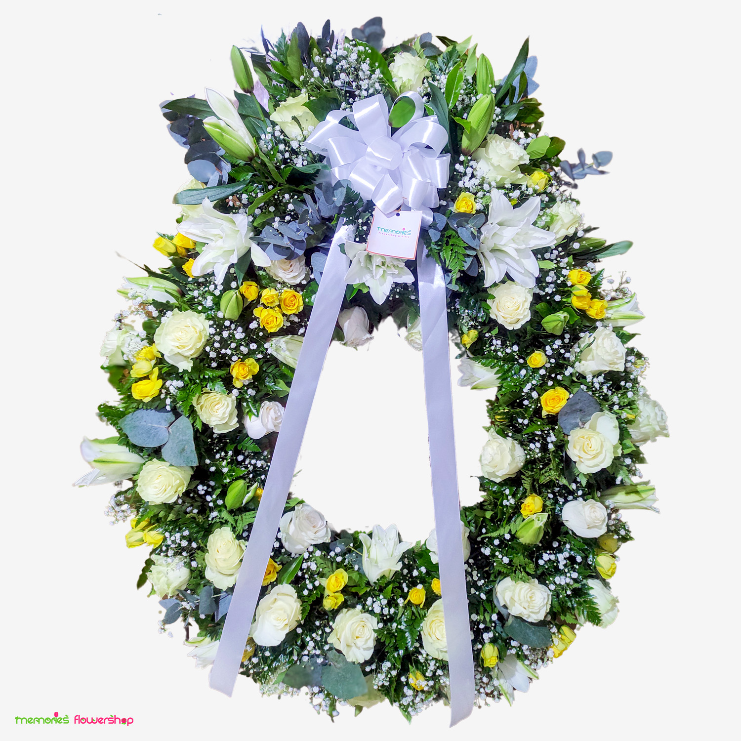 Elegante corona grande con penacho de rosas blancas, mini rosas amarillas, lirios y eucalipto, ideal para expresar condolencias con delicadeza y respeto. Corona grande con penacho de rosas blancas, mini rosas amarillas, lirios y eucalipto
